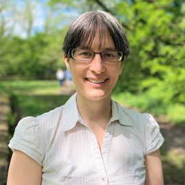 Dr Heather Turner outside in the sun, smiling. She is a white woman in her 40s with dark straight hair tied back and wears glasses. She is dressed in a business casual shirt.